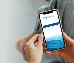 A photo of a hand holding a smartphone featuring the TFS app.